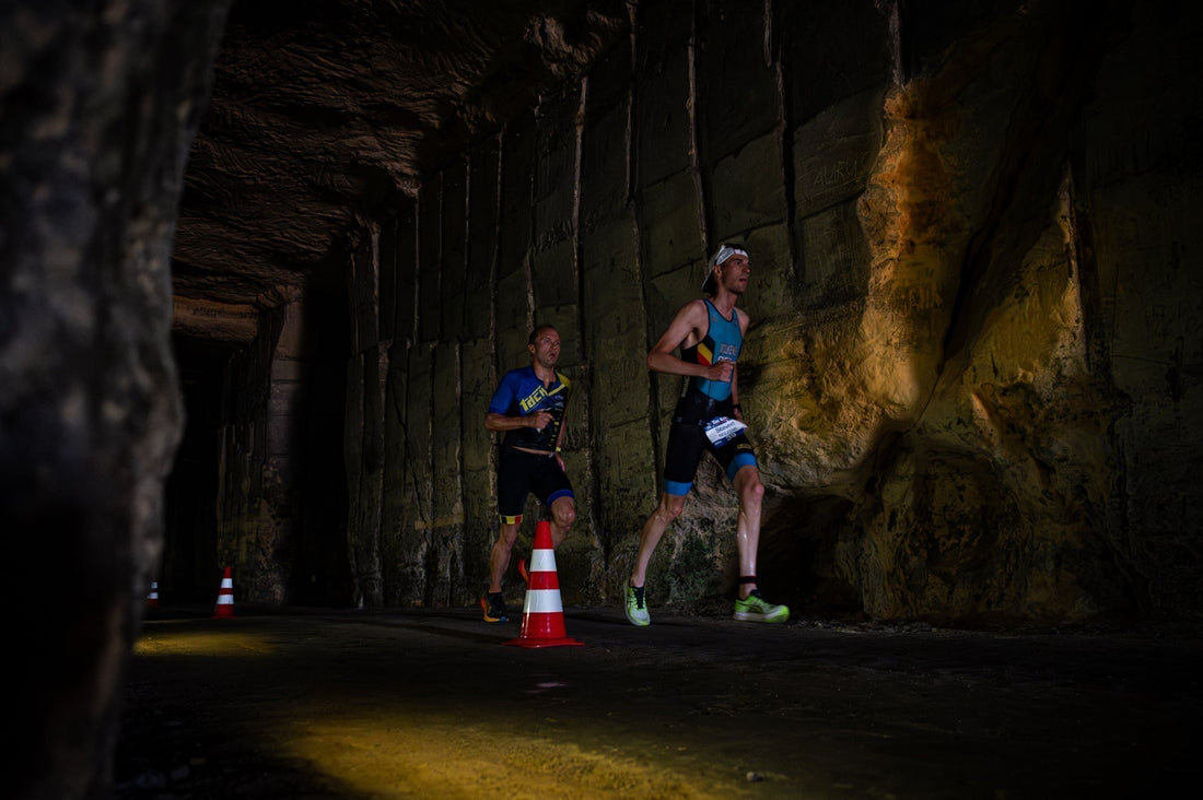 Two runners in a dark tunnel with minimal lighting during the cave triathlon